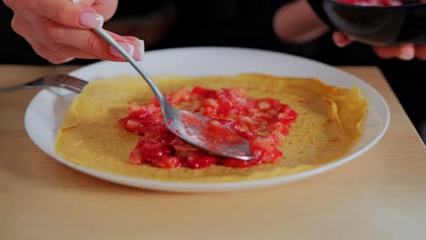 homemade crepe topped with vibrant berry purée on white plate at wooden table