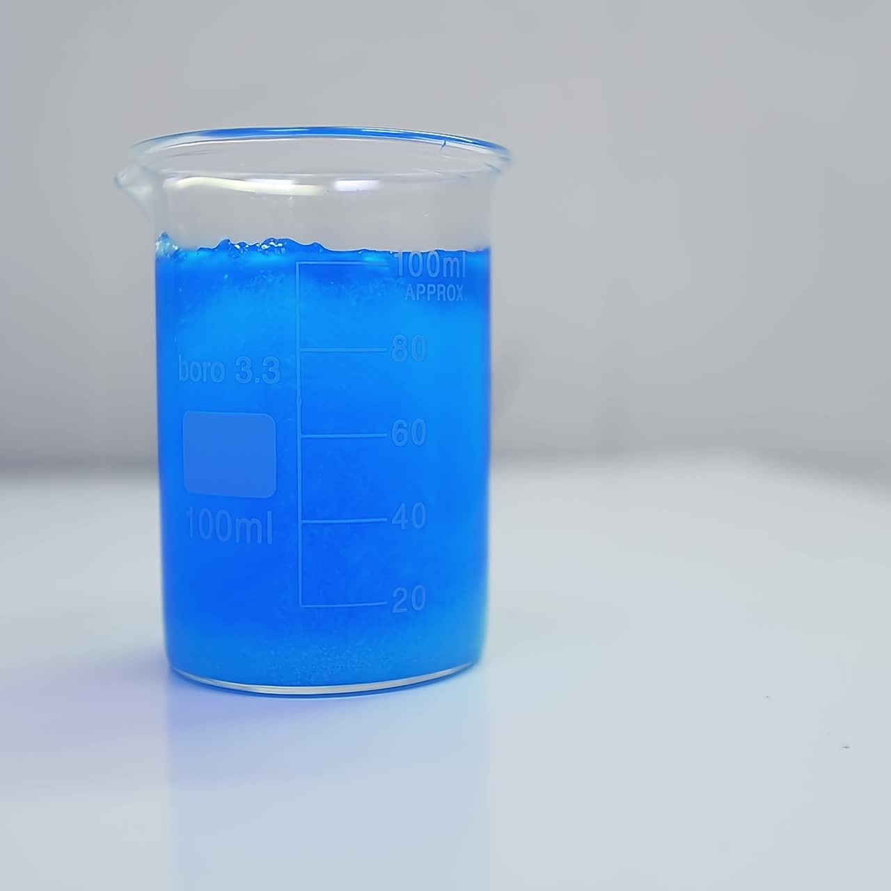 Hand of researcher pours blue liquid into the beaker with diaper filler. Blue liquid mixes up with filler and interacts with it. Close up