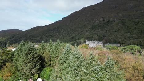 Aerial-ascending-revealed-shot-of-the-historic-and-oldest-Benedictine-Abbey-the-Kylemore-Abbey-in-Connemara-Galway,-Ireland-overlooking-a-black-river-which-mirrors-the-abbey