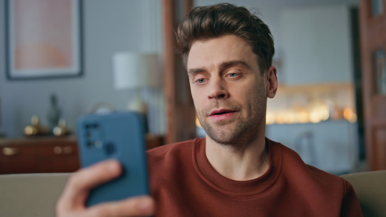 Serious man talking webcam chat by smartphone on couch close up. Guy video call