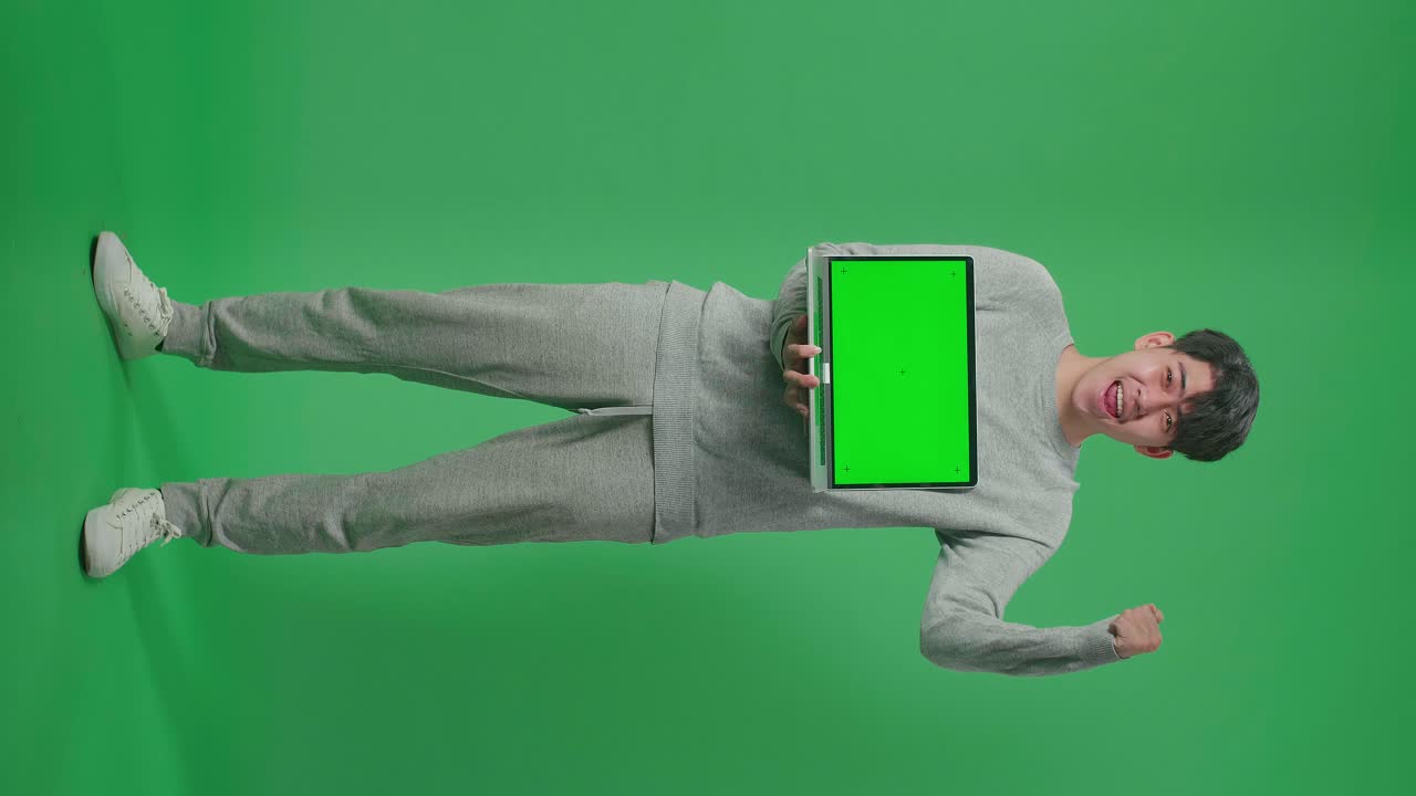 Full Body Of Happy Asian Man Celebrating While Holding Green Screen Computer In The Green Screen Studio