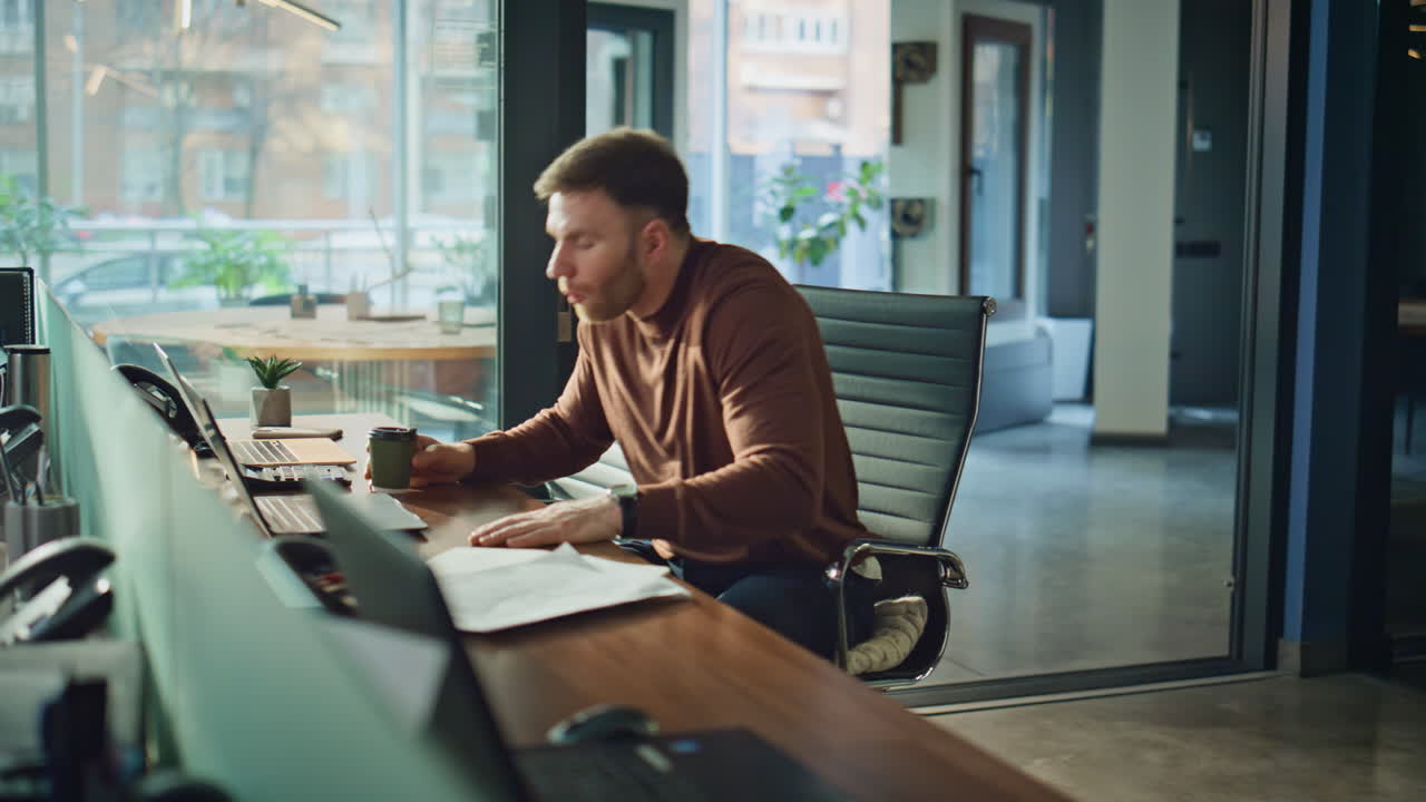 Serious professional drinking coffee at desk in office. Thoughtful male employee