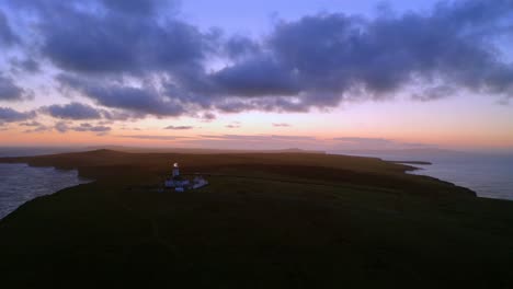 aerial dolly glides over loop head peninsula at warm twilight, with lighthouse lights spinning beautifully