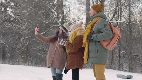 father, mother and daughter taking photos with smartphone in a snowy forest