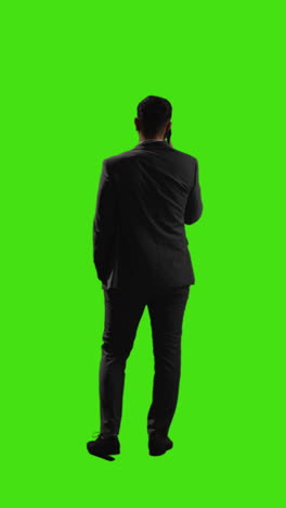 Vertical-Video-Rear-View-Of-Businessman-Standing-Talking-On-Mobile-Phone-Against-Green-Screen-Background