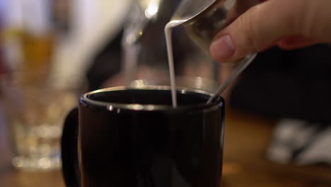 pov perspective of pouring milk into a black coffee mug