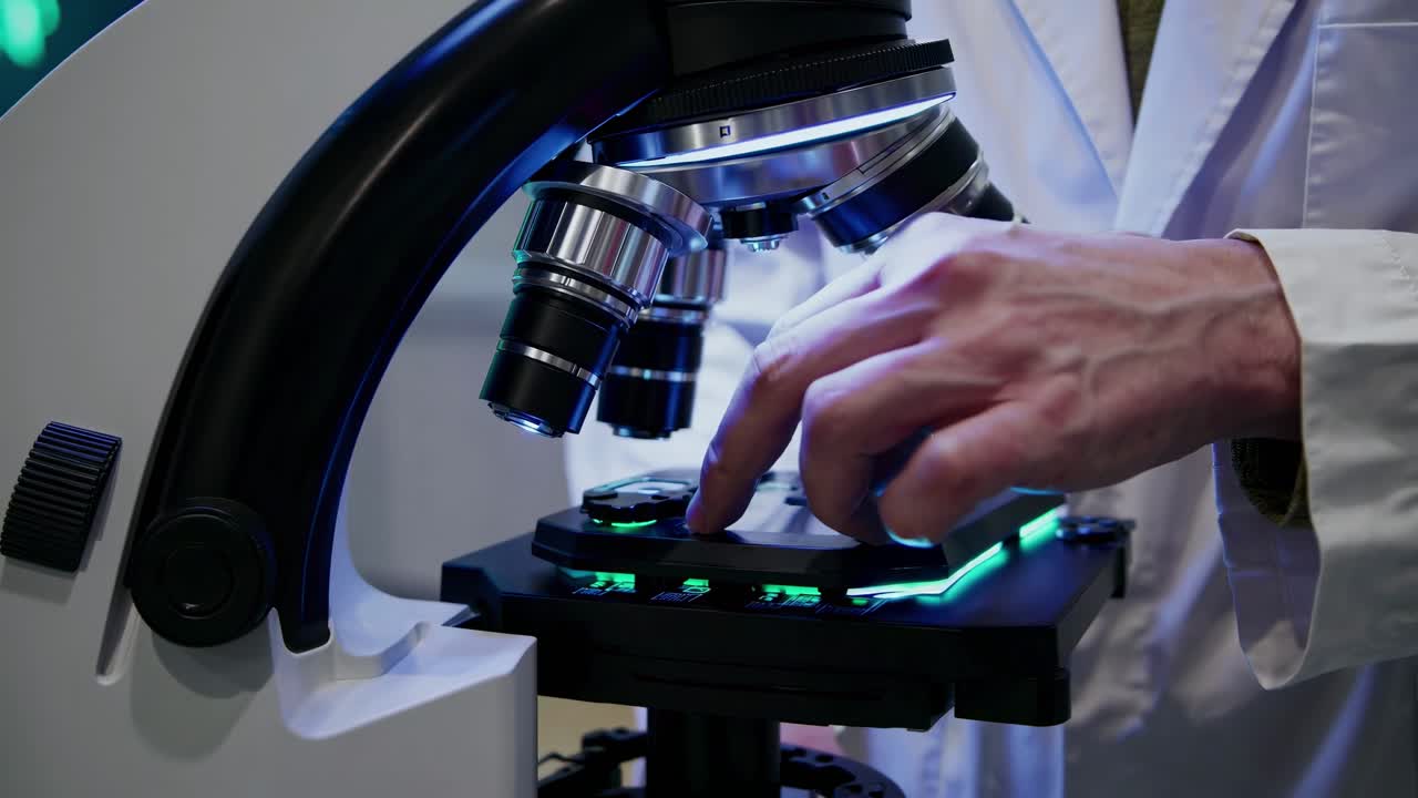 Close-up video angle of a scientist's hand adjusting a microscope, highlighting precision
