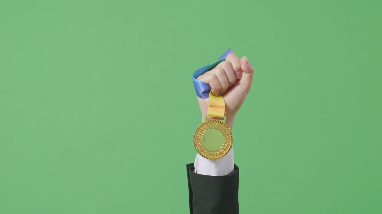 cerca de la mano del hombre de negocios sosteniendo una medalla de oro en el aire para celebrar la victoria como el primer ganador en el fondo de la pantalla verde en el estudio