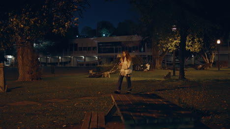 brunette strolling dark park with smartphone in hand. woman typing on mobile