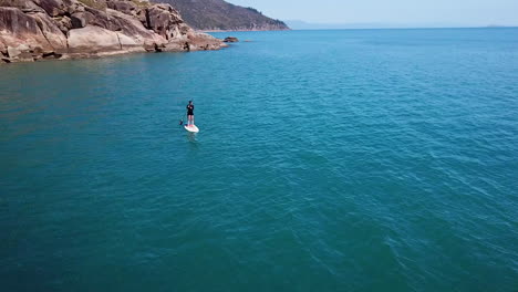 Aerial-drone-footage-circling-around-lone-female-paddleboarding-towards-luxury-yacht-at-remote-island-destination