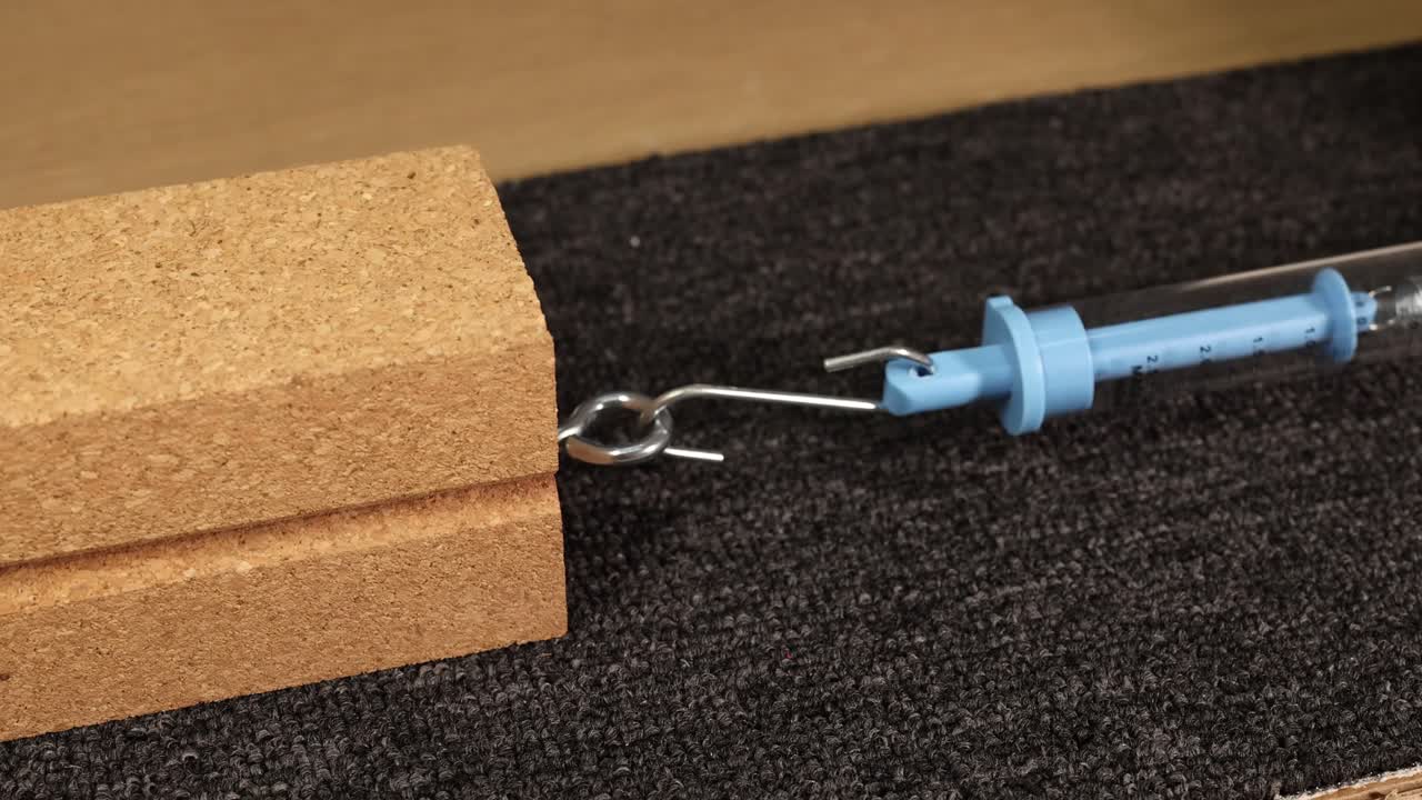 A hand uses a spring scale to measure the friction force of a wooden block on carpet