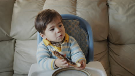 asian baby eats pizza, sits on the baby's feeding table