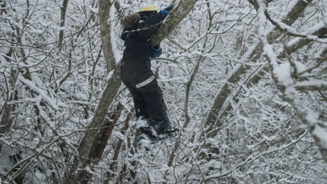 Junge-Klettert-Im-Verschneiten-Baum-Und-Spielt-Draußen,-Fällt-Im-Winter-Vom-Baum