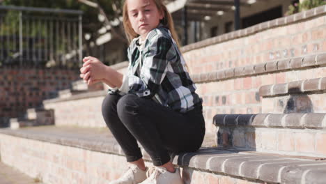 young girl sitting on outdoor steps, wearing casual clothes, enjoying sunny day, at school
