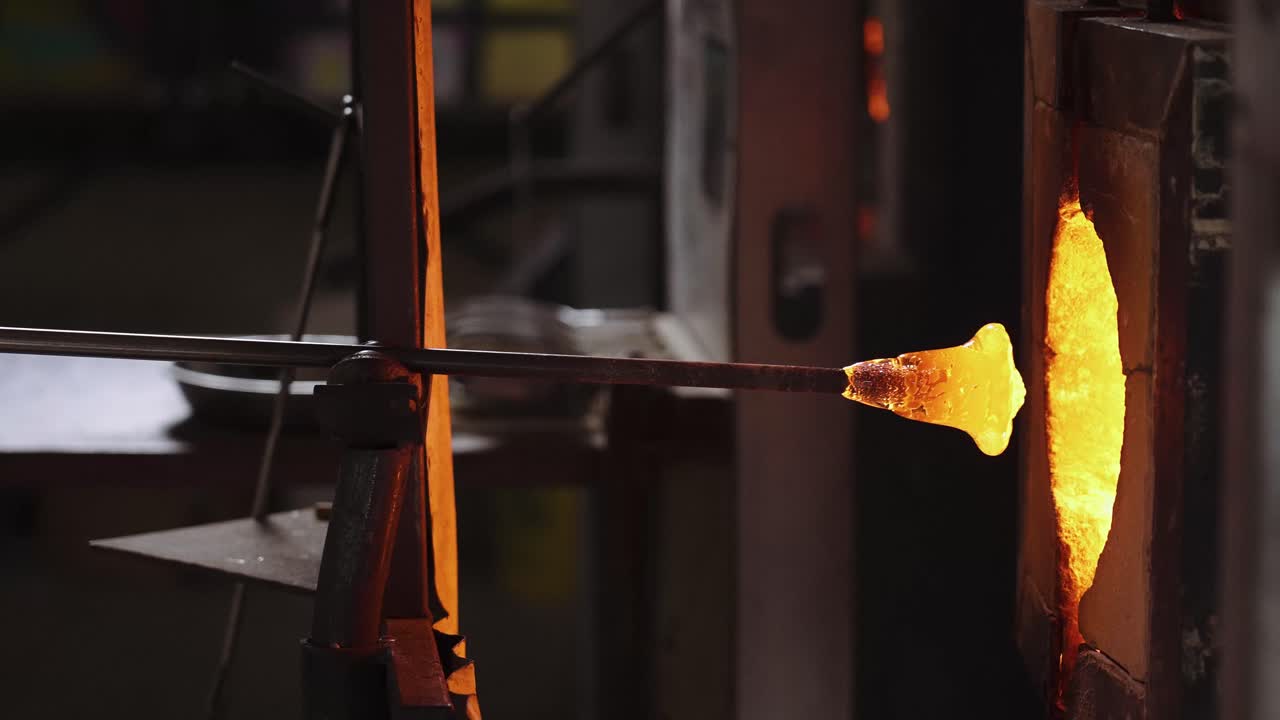 A glass blower pulling a glass cup from a high-powered furnace.