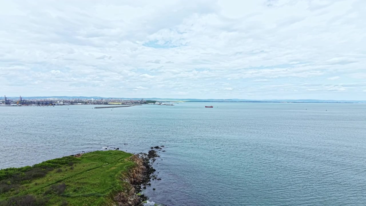 Vista della costa con l'acqua che si estende fino all'orizzonte e lo skyline della città sullo sfondo in una giornata nuvolosa.