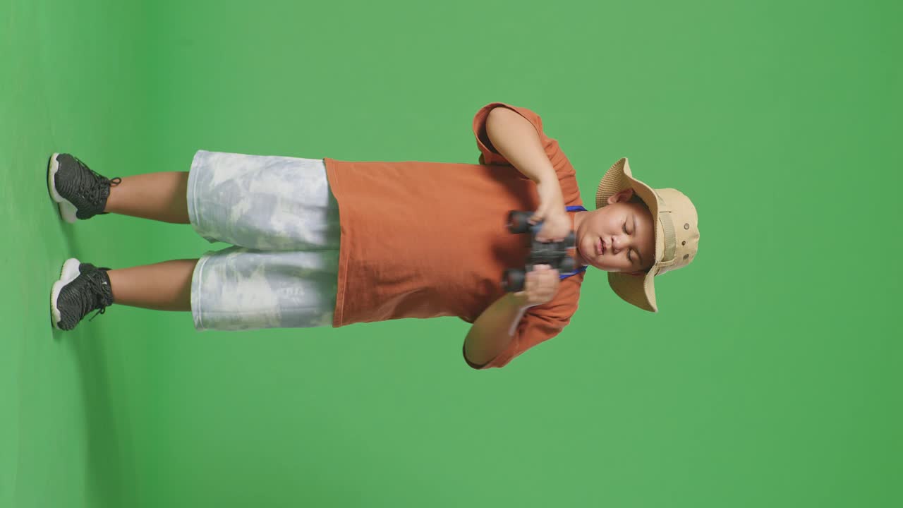 모자를 입은 아시아 관광 소년은 을 흘린 얼굴을 고 안경을 통해 보았다. 소년 연구원은 녹색 화면 배경에서 무언가를 조사합니다. 여행 관광 모험 개념, 전체 몸.