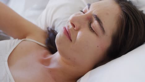 Confused-caucasian-woman-lying-in-bed-and-covering-her-eyes-with-arm