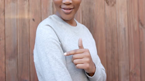 feliz mujer afroamericana en sudadera gris apuntando a la manga, cámara lenta, espacio de copia