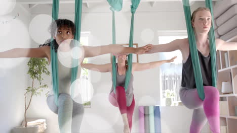 animation of light spots over diverse female instructor and teenage girls practicing aerial yoga