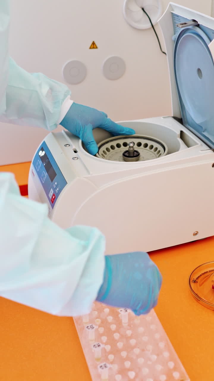 Laboratory assistant near automated device for making analysis. Female worker in protective uniform takes out test tubes from centrifuge in lab. Vertical video
