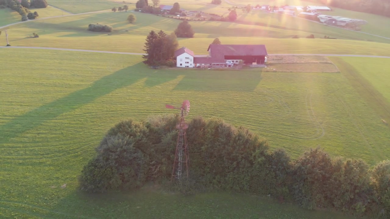 Droneflyvning omkring en vindmølle med solen gående ned bagved.
