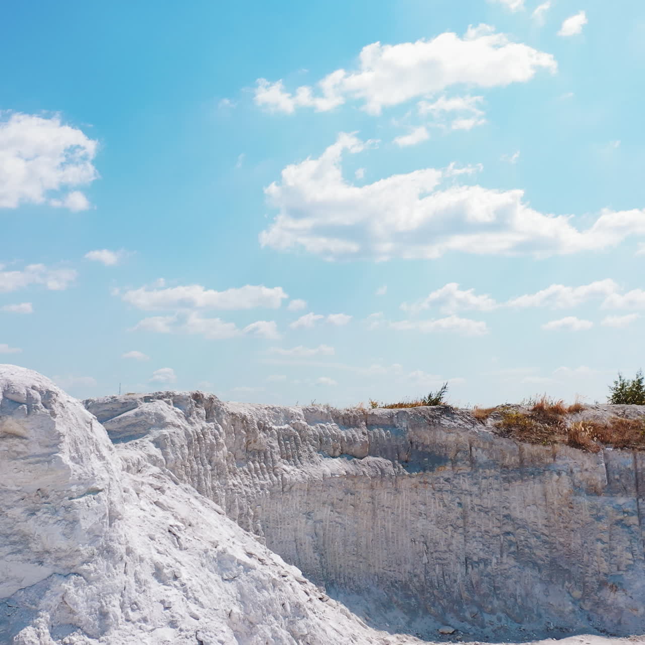 Sporty man drinks water outdoors. Athletic man standing on the top of white hill and drinking after training in summer. Camera moves around.