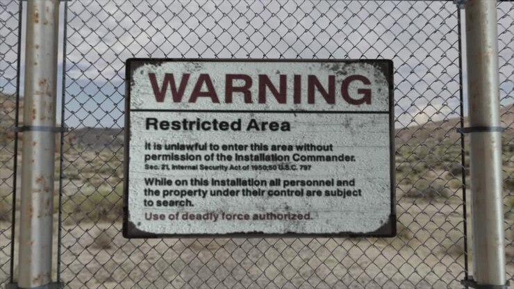 Render CGI 3D di alta qualità con una fluida carrellata in avvicinamento di una recinzione a rete metallica presso un'installazione ad alta sicurezza in una scena desertica, con un cartello "Attenzione: Area Riservata"
