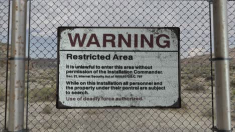 high quality 3d cgi render with a smooth dollying-in shot of a chainlink fence at a high security installation in a desert scene, with a warning restricted area sign