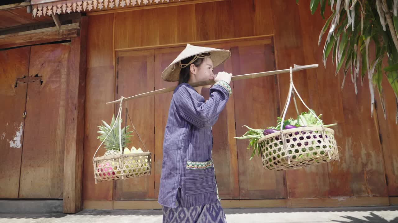 Woman carrying fruits and vegetables on a pole in a local market.