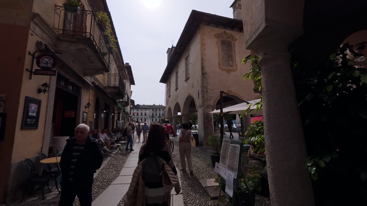 Charming cobblestone street scene in Orta San Giulio, Italy, showcasing rustic arches, historic architecture, and people enjoying a leisurely stroll in this quaint Italian village