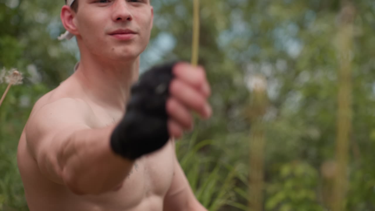 Tourist wearing glove and headband extends arm forward with intense expression to pluck dandelion from lush field, background filled with vibrant greenery and blurred flowers under soft daylight sky