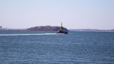 tug boat moving away from camera with island peninsula in the background