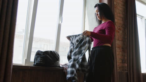 young woman folding plaid shirt by a window