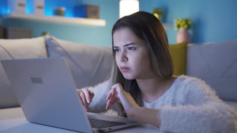 young woman using laptop with focused and serious expression.