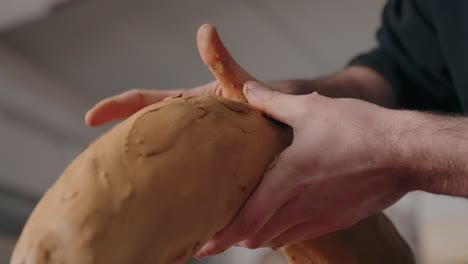 close up of hands shaping curved clay surface in soft daylight during sculpting