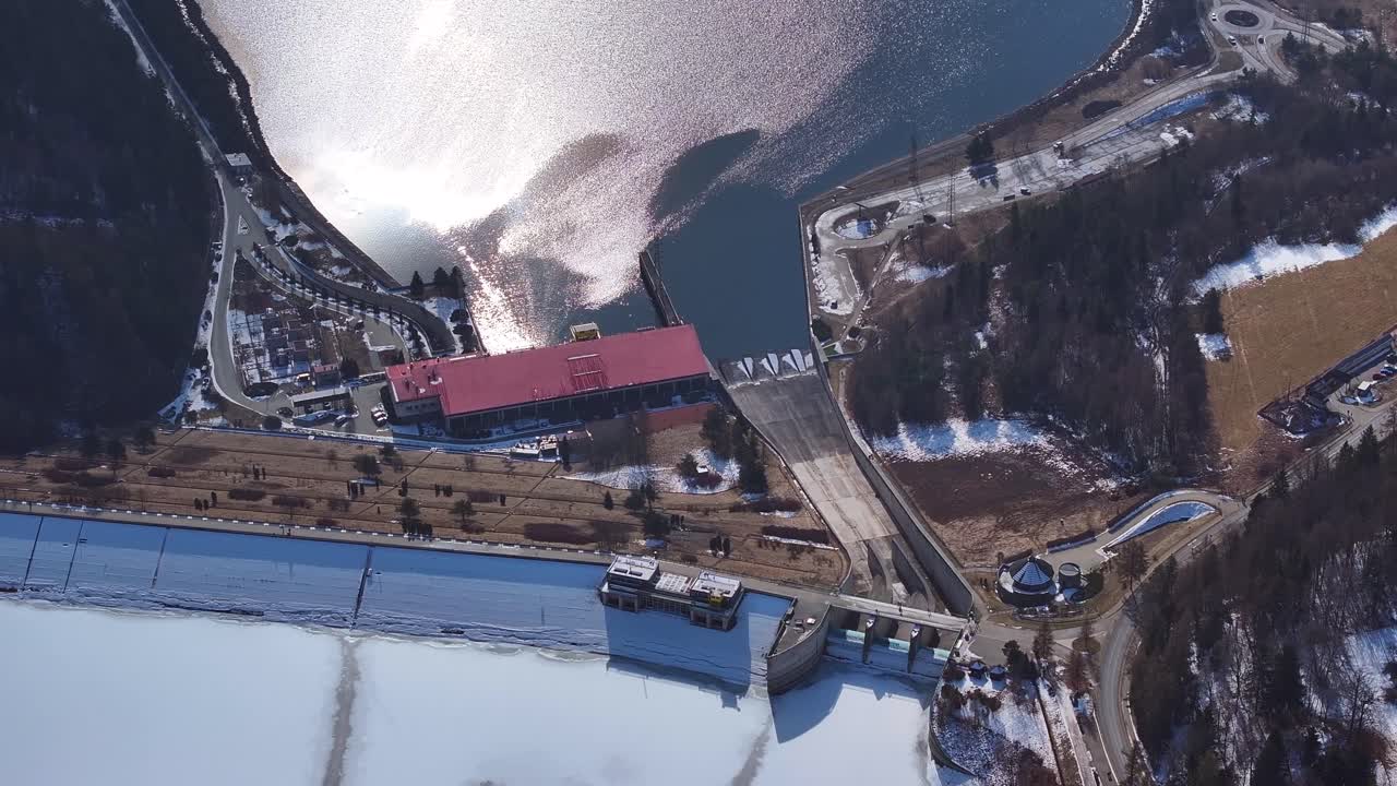 Vista aerea di un paesaggio innevato che mostra strutture industriali vicino a un lago sereno sotto la luce solare invernale.