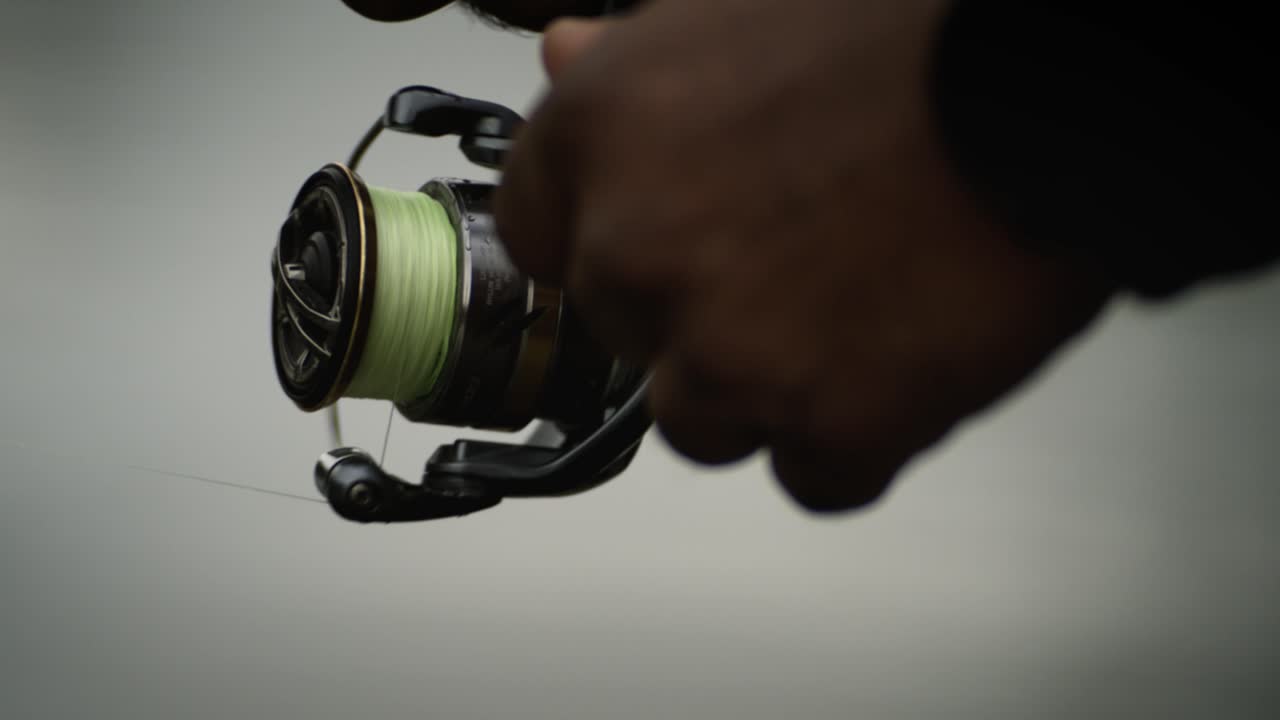 Primo piano: pescatore che avvolge il mulinello e recupera la lenza, super slow motion.