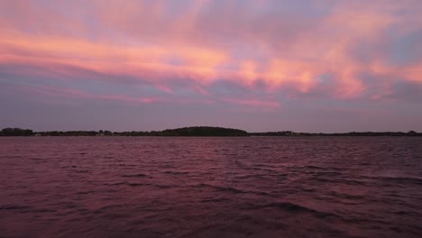 vista cinematográfica de drones sobre un lago que muestra un cielo rosa, azul y blanco con un bosque en el fondo
