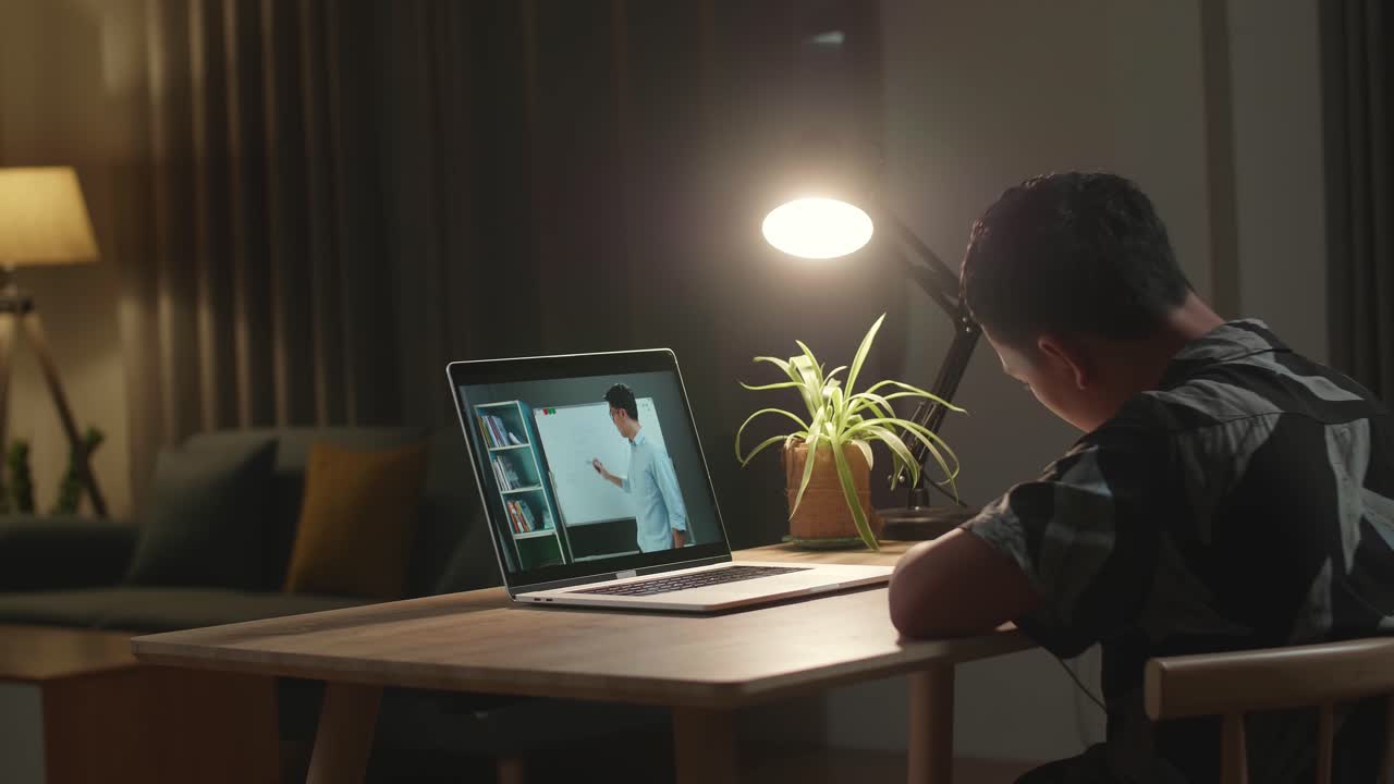 Asia Teen Boy Student Distance Learning With Online Teacher On Computer Screen From Home At Night