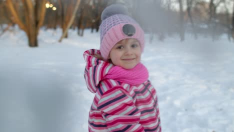 Smiling-child-kid-girl-throws-snowball-into-camera,-having-fun,-fooling-around-in-winter-park-forest