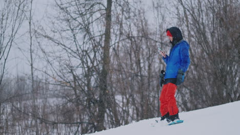 male snowboarder rides the board at the ski to the snow slope and writing messages to smartphone to your friends