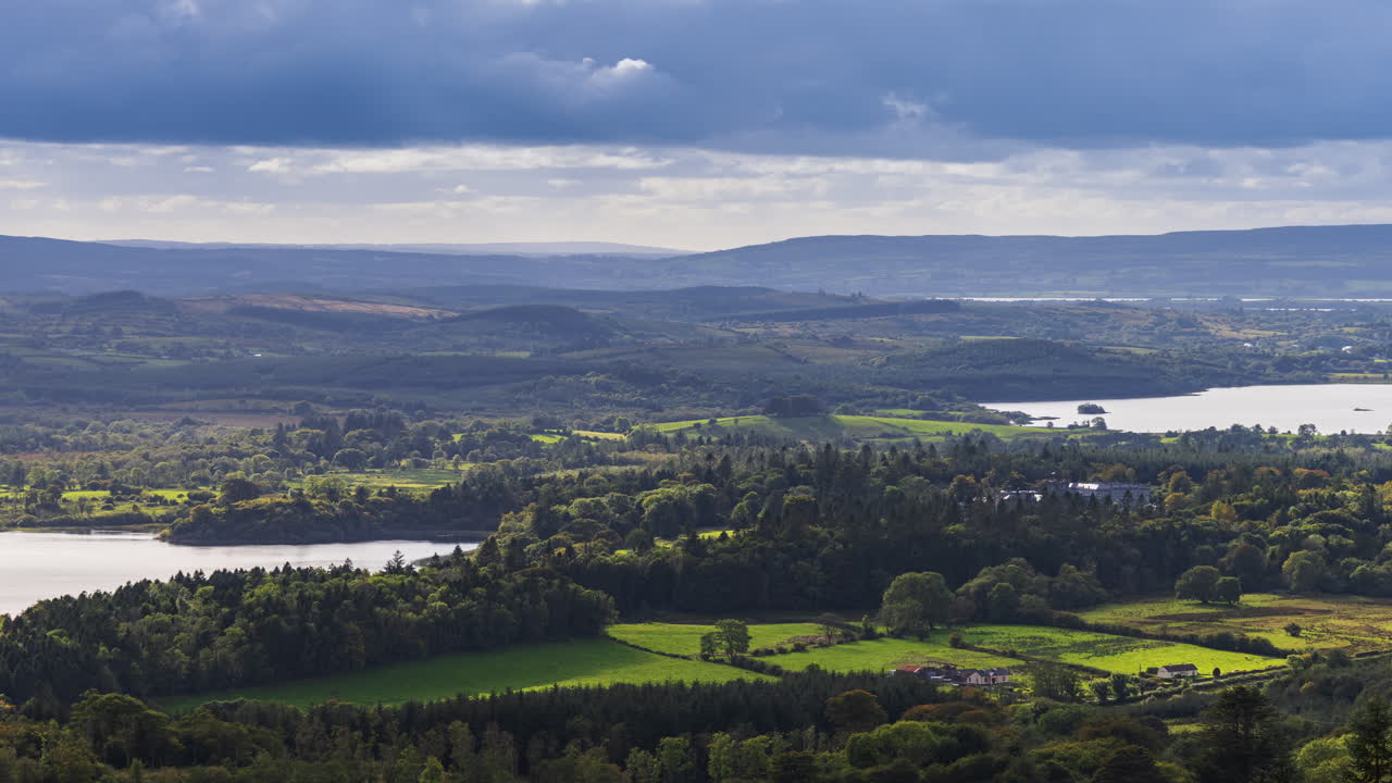 Time lapse of rural landscape with Kilronan castle in the distance surrounded by lake, forest and hills during a cloudy day viewed from above Lough Meelagh in county Roscommon in Ireland