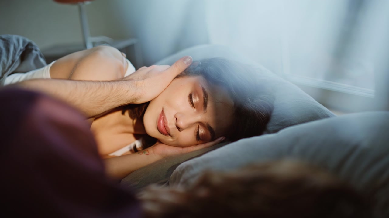 Donna al mattino che accarezza un uomo assonnato sdraiato tra le lenzuola, primo piano. Fidanzata innamorata