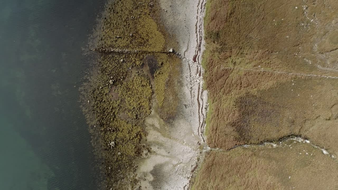Topdown aerial tracking over the edges of a loch with autumn shade coastline