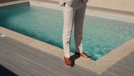 man in beige formal trousers and polished brown shoes standing beside a luxurious swimming pool with clear blue water