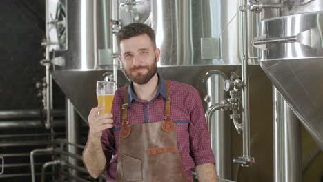 young brewer wearing a leather apron is tasting beer at a modern brewery