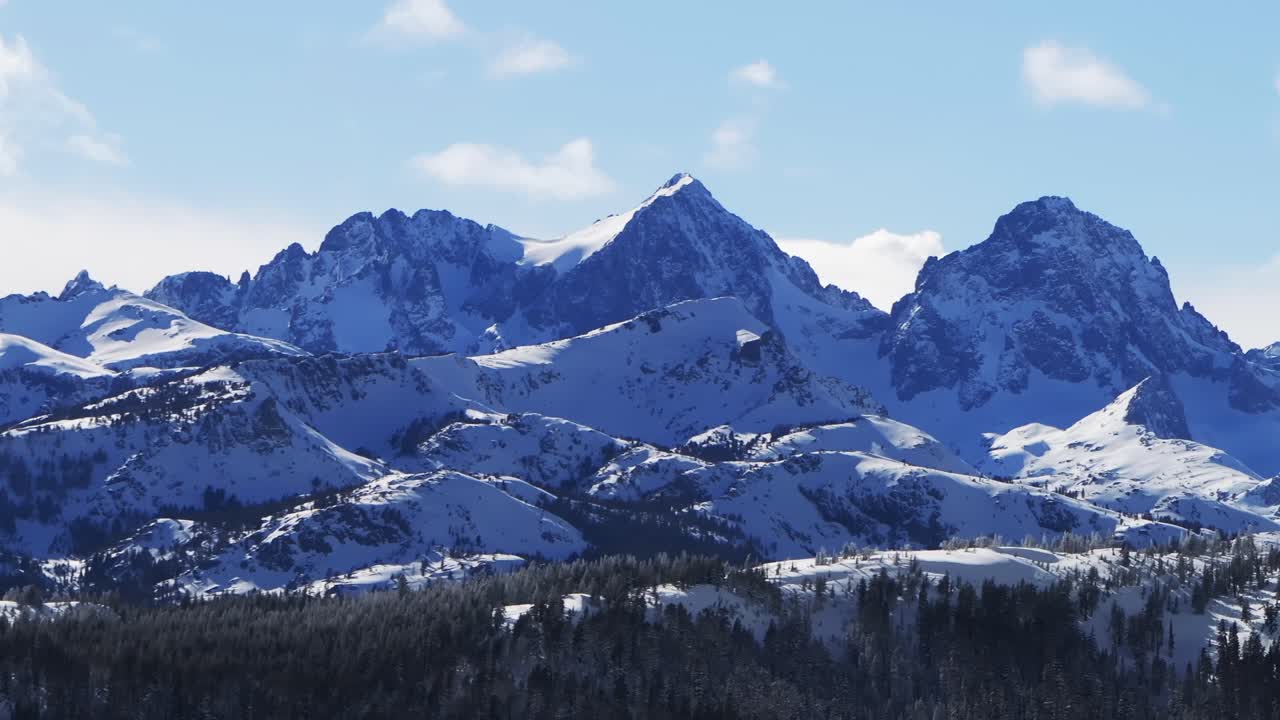 Das Hemlocks Mammoth Mountain Ski- und Snowboardresort, Drohnenaufnahme, Kalifornien. Die zerklüfteten, aufragenden Gipfel der Minarets, ziehende Wolken, Winter, sonniger blauer Himmel am Nachmittag, frischer Tiefschnee, statische Aufnahme.