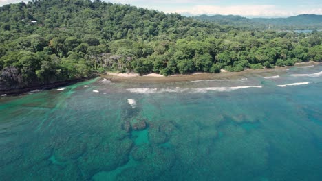 drone pan right movement capturing cocles beach's shoreline, turquoise waters, and distant tropical hills in costa rica.