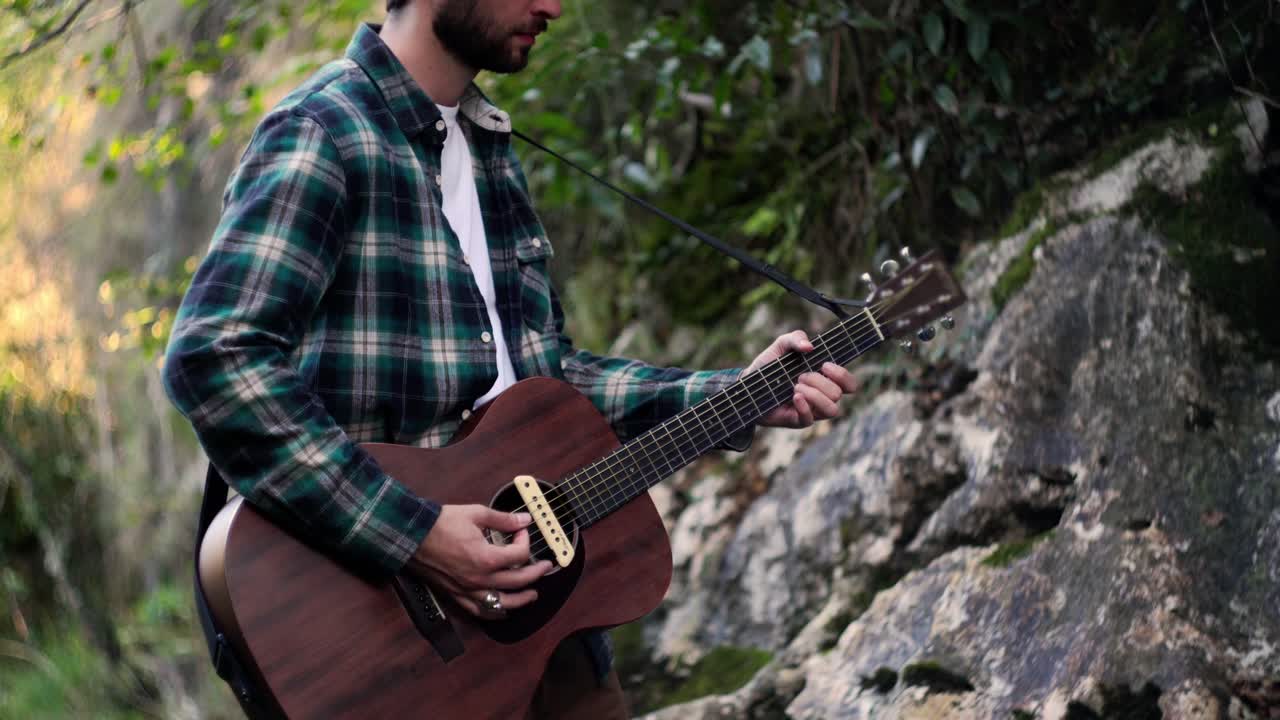 músico folclórico tocando música con guitarra acústica en un bosque verde
